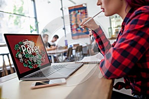 Side view of a young pink hair woman keyboarding on laptop computer with poker online on a screen while sitting in cafe.