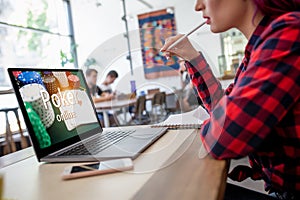 Side view of a young pink hair woman keyboarding on laptop computer with poker online on a screen while sitting in cafe.