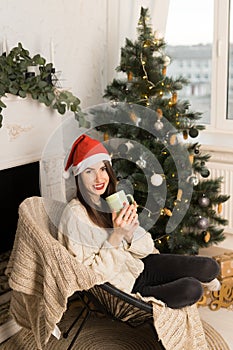 Side view of a young smiling girl holding a green cup of cacao near Christmas festive tree