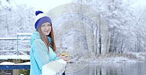 Side view of young smiling woman with a cup of hot tea or coffee on snowy winter waterside.