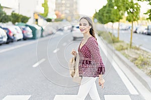 Side view of young trendy ethnic female with makeup and cigarette walking on road in city while looking at camera