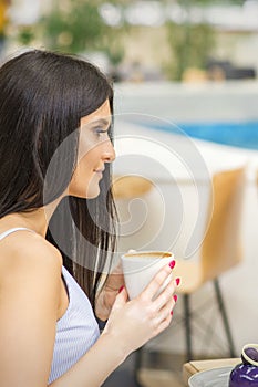 The side view of a young woman drinking coffee resting at the resort at a cafe outdoors.