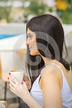 The side view of a young woman drinking coffee resting at the resort at a cafe outdoors.