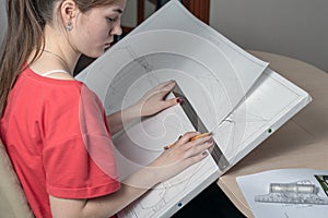 Side view of a young woman with a graphics tablet draws a sketch with a ruler and a pencil