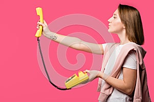 side view of young woman holding yellow rotary phone isolated