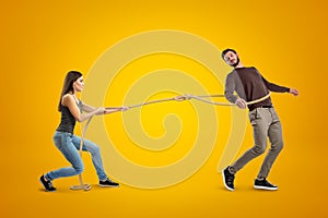 Side view of young woman lassooing young man on yellow background.