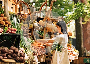 Side view of a young woman in an outdoor market. Female with shopping bag buying fresh vegetables