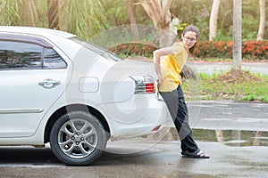 Side view of young woman pushing broken car on the road.