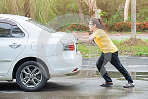 Side view of young woman pushing broken car on the road.