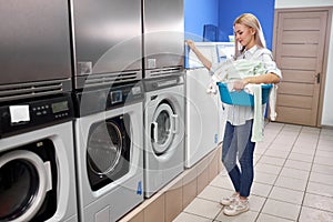 side view on young woman standing alone with dirty clothes in the self serviced laundry with dryer machines