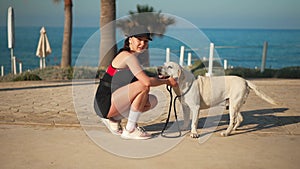 Side view young woman stroking white dog at background of picturesque Cyprus landscape. Relaxed happy Caucasian tourist
