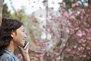 Side view of young woman talking on the phone outdoors in the park in springtime