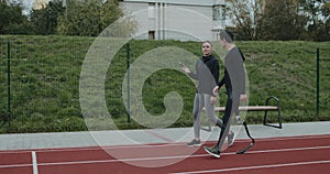 Side view of young woman talking to man with prosthetic running blade outdoors. Female person chatting with male athlete