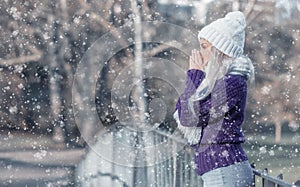 Side view young woman warming her hands, wears warm clothing on snowing winter day outdoors. Cute girl feeling cold. Winter