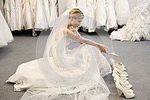 Side view of young woman in wedding dress confused while selecting footwear