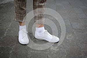 Side view of young women`s foot in white sneakers on asphalt background.