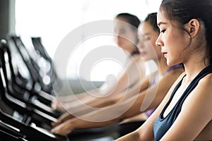 Side View Of Young Women Sitting On Exercise Bikes In Gym