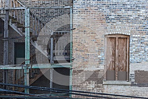 Side of vintage brick building with wooden fire escape staircase protected by chicken wire in Chicago