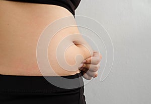 Side of woman hand catching fat body belly paunch , diabetic risk factor .