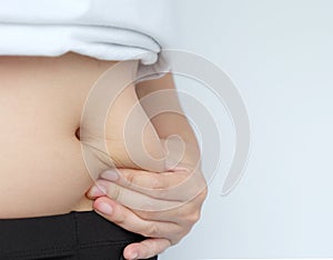 Side of woman hand catching fat body belly paunch , diabetic risk factor .