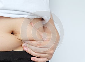 Side of woman hand catching fat body belly paunch , diabetic risk factor . photo