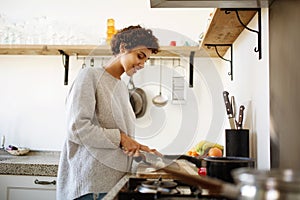 Side of young woman cutting vegetables with knife in kitchen