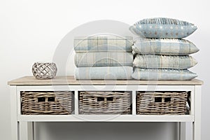 Sideboard style white wooden table with blue coloured cushions, throws and ornaments and wicker baskets on white