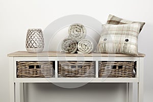 Sideboard style white wooden table with natural coloured cushions, throws and ornaments and wicker baskets on white