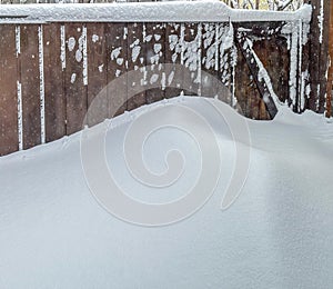 Sidelight snow bank against wood fence. Snow has drifted and looks like ocean wave.