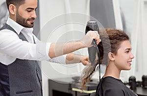 Sideview of Arabian hairstyler drying smiling female client`s curly hair.
