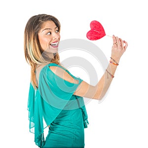 Sideview of beautiful woman holding red heart-shaped lollypop in front of her body