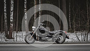 Sideview of a black motorcycle cruiser on a background of a winter forest