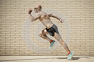 Sideview of a fit athlete running in the street without shirt. Muscular man trainning and sprinting in a city.