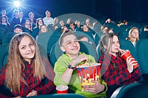 Sideview of girls and boy eating popcorn by watching movie.