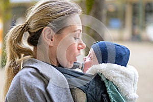 Sideview of a late-term mother in her 40s lovingly holding her newborn baby in a baby carrier