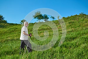 Sideview of old man walking with tracking sticks in mountains.