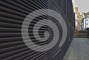 Sidewalk and black wall with large air conditioning vents that form converging lines leading towards distant steps