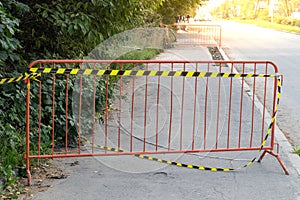 sidewalk blocked by a metal fence with yellow black warning tape