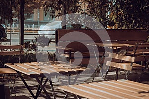 Sidewalk cafe. Modern urban public place. Wooden chairs and table in patio under the trees. Outdoor furniture. Modern lifestyles