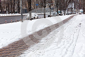 The sidewalk cleared of snow runs along the carriageway of the city street