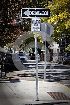 Sidewalk Dismount Zone for bikes and scooters sign on busy shaded autumn street