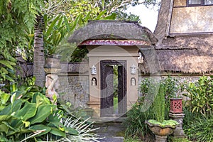 The sidewalk leads to a enter in house with Balinese sculptures in a tropical garden, island Bali, Indonesia