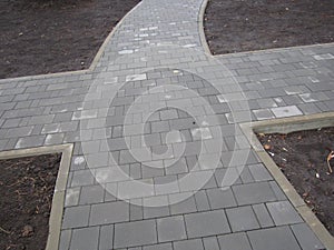 sidewalk lined with gray tiles and black lawn soil