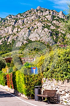 Sideway of a road with wooden bench, dead end road sign, shaped hedge on stone fence and private houses, hotels of a beautiful