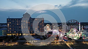 sideways aerial footage of the Carolina Beach Boardwalk with a Ferris wheel, colorful amusement rides, people walking