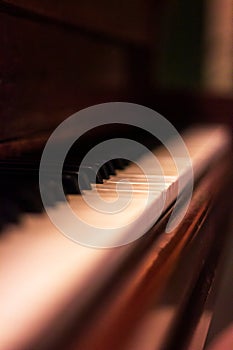 A sideways portrait of the white and black keys of a beautifful old wooden piano. Some of the keys are worn out or have fallen off