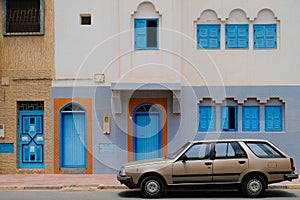 Sidi Ifni, Morocco - vintage bronze station wagon car parked outside a white building with bright blue doors and quirky windows.