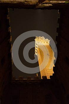 Siena at night. Tower of Mangia seen from below and illuminated by the colors red and white in the center of the roofs.
