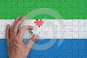 Sierra Leone flag is depicted on a puzzle, which the man`s hand completes to fold