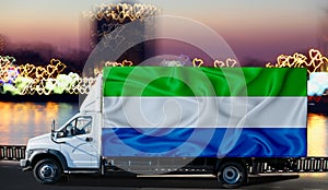 Sierra Leone flag on the side of a white van against the backdrop of a blurred city and river. Logistics concept